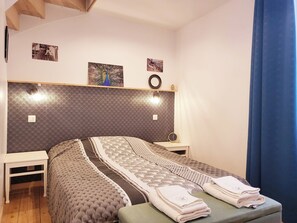 Une chambre à coucher bien rangée, avec une tête de lit à motifs, un lit recouvert d’une couvre-lit décorative, deux tables de chevet avec des lampes et une horloge fixée au mur.