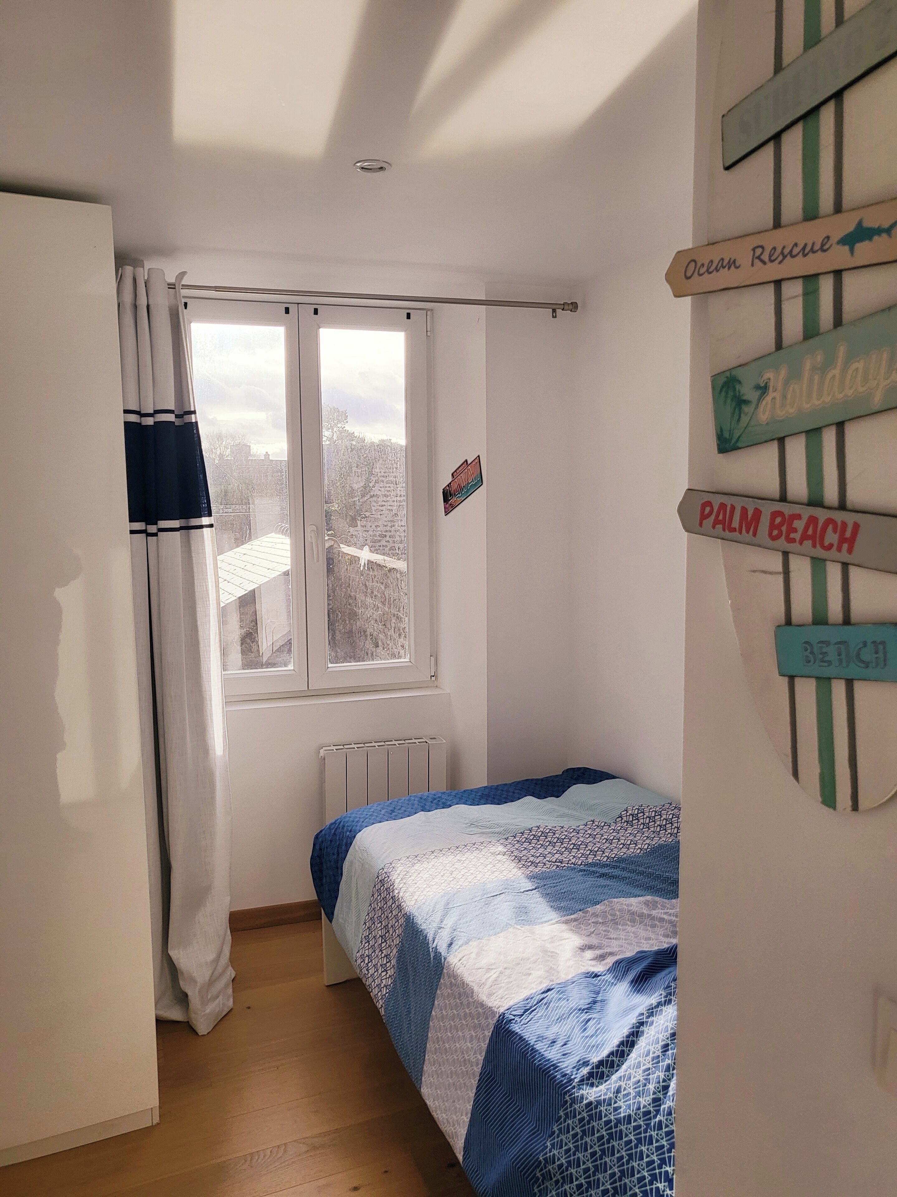 A bedroom with a bed, a window, a radiator, and a wall with directional signs.