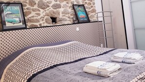 Een slaapkamer met een stenen muur, een bed met beddengoed met een patroon, en twee ingelijste foto's aan de muur.