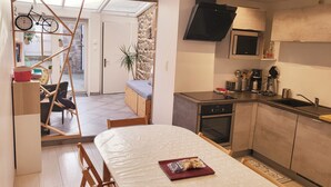 Een kleine keuken met een magnetron, koffiezetapparaat en een spoelbak. Er is een eethoek met een tafel en stoelen, en een zithoek met een bank en een fietsdecoratie.