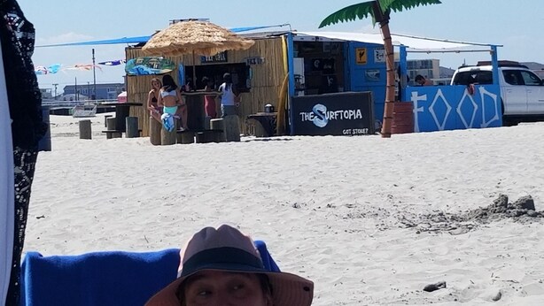 Uno stand gastronomico sulla spiaggia con un cartello che riporta 'THE SURFTOPIA'.