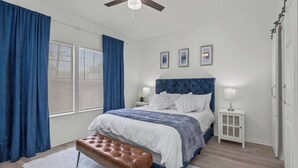 Una camera da letto con un letto grande, un ventilatore a soffitto, un comodino con una lampada e una finestra con persiane.