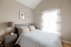 Un dormitorio con cama, mesita de noche, lámpara y dos cuadros en la pared.