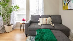 A living room with a gray sofa, a green throw blanket, a potted plant, and a painting on the wall.