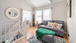 A living room with a grey sofa, a green throw, a round mirror, and a staircase.