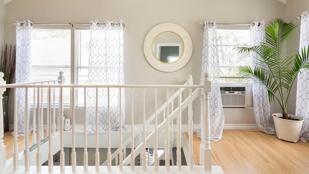 A staircase with white railings, a round mirror on the wall, and a potted plant.