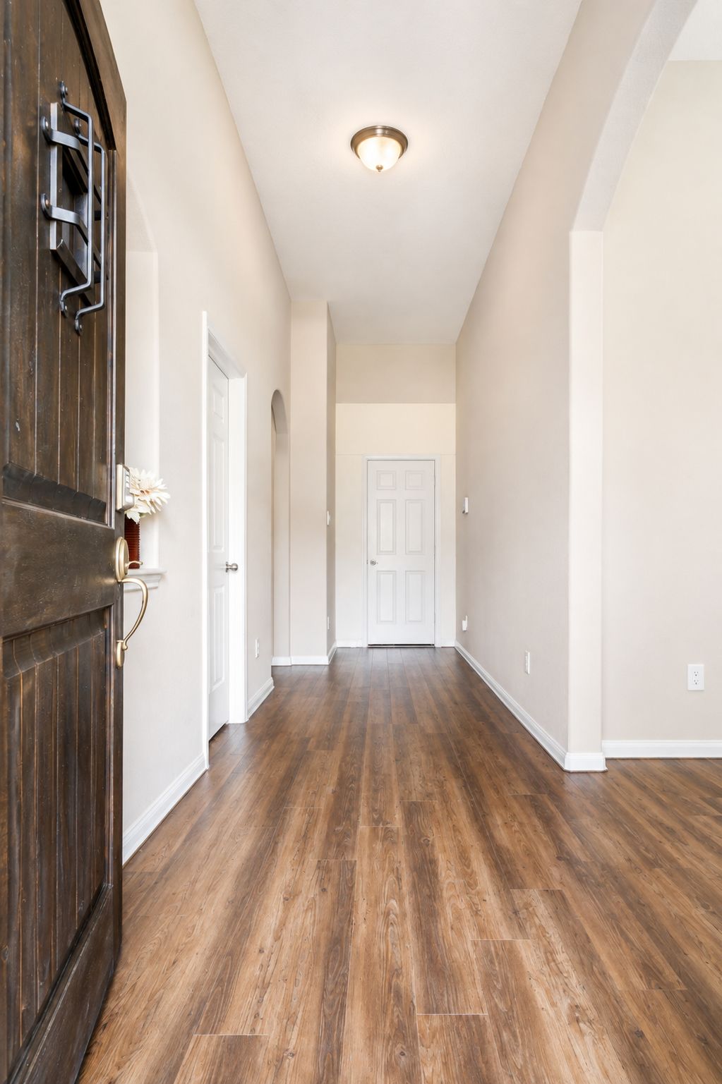 A hallway with wooden flooring, white walls, and a white door at the end.