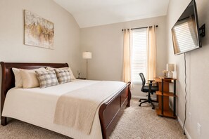 A bedroom with a bed, a desk, a chair, a lamp, and a TV mounted on the wall.