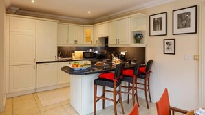 Una cocina moderna con armarios blancos, una isla central con taburetes altos y un comedor con sillas anaranjadas.