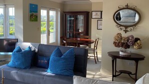Una sala de estar con sofá, una mesa de comedor y sillas. Hay un televisor, una chimenea y un ventanal con vistas a zonas verdes.