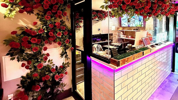 Un espace d’accueil avec un comptoir en briques, un téléviseur fixé au mur et un grand arrangement floral composé de roses rouges.