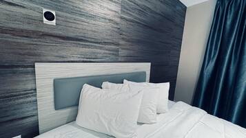 Une chambre d’hôtel moderne avec un mur en bois, une tête de lit et un lit recouvert de linge de lit blanc.