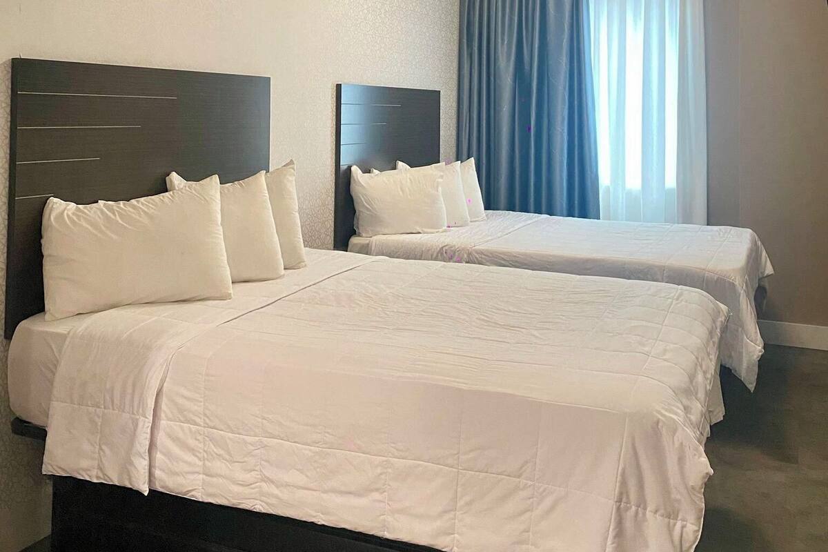 A hotel room with two beds, a headboard, a window with curtains, and a ceiling light fixture.