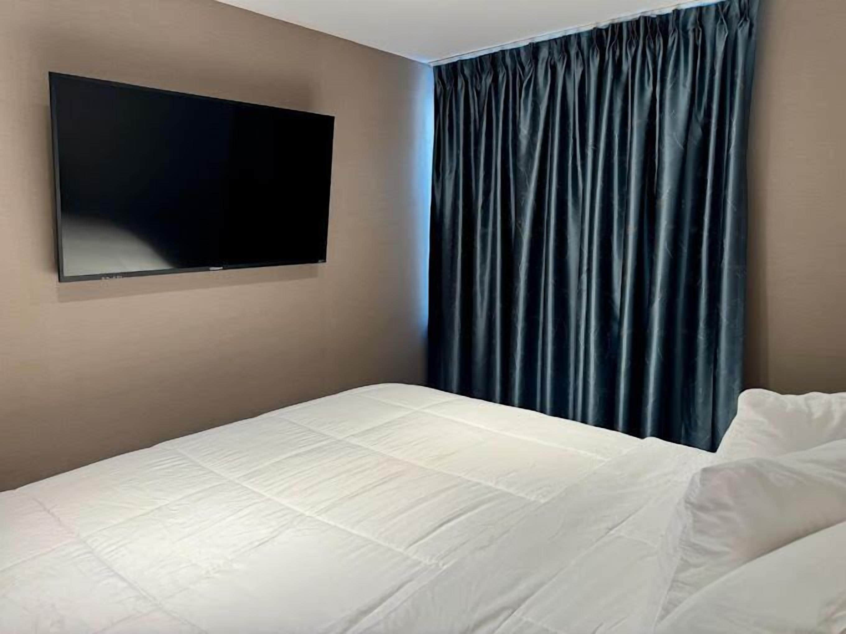 A hotel room with a bed, a flat-screen TV mounted on the wall, and a dark blue curtain.