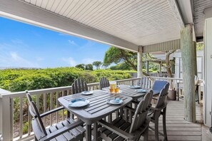 An outdoor patio with a table set for two, a chair, and a view of the landscape. - Exclusive Seascape in West Beach Village! 3 King Beds! Oceanfront! (Kiawah Island)
