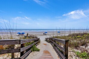 A wooden pathway leading to beach umbrellas on a sandy beach.