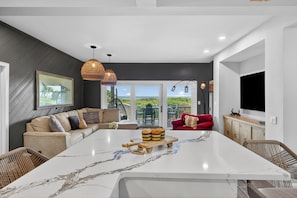 A modern kitchen with a marble island, wicker furniture, and a large window with a view.