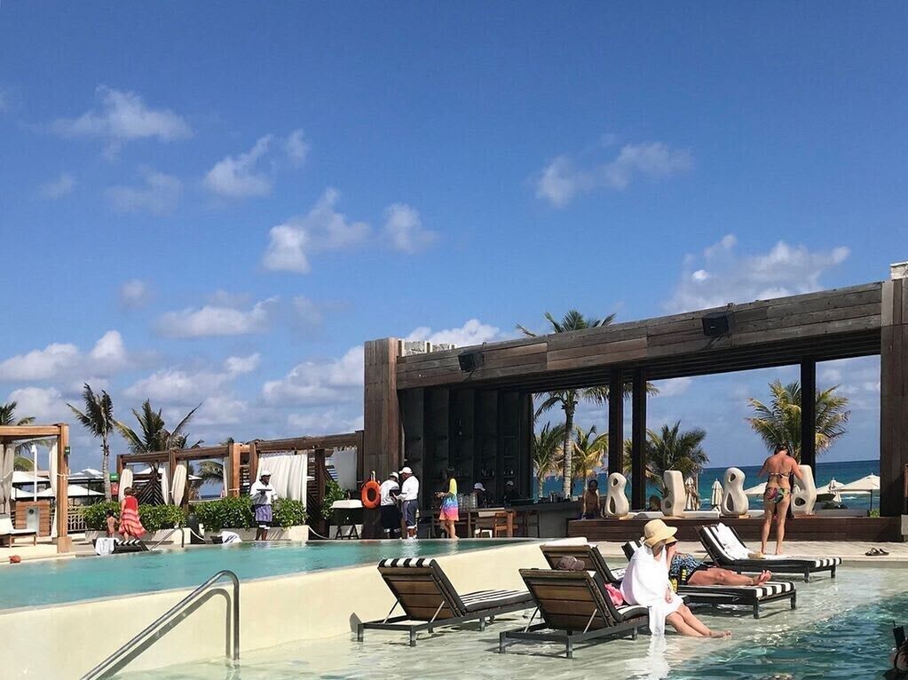 A pool area with lounge chairs, a wooden pergola, and palm trees.