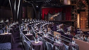 A theater with rows of tables and chairs, a stage with red curtains, and a large dragon mural on the wall. - 2BD Grand Bliss Vidanta Resort RM (Playa del Carmen)