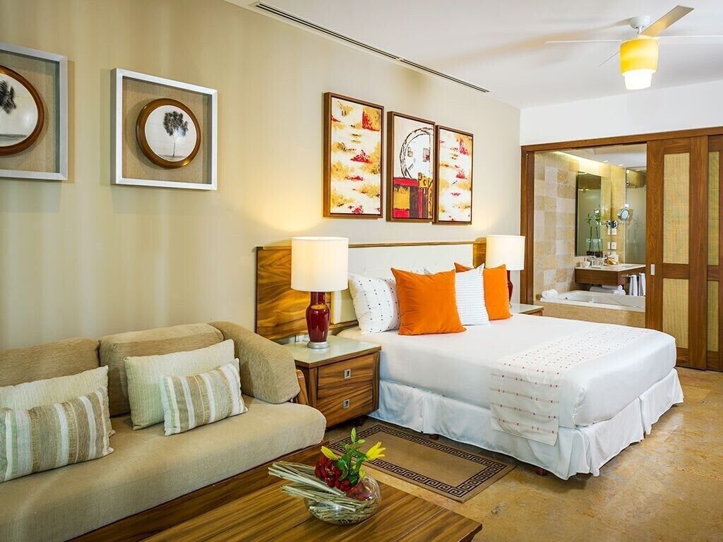 A hotel room with a bed, a sofa, a nightstand, and artwork on the wall.