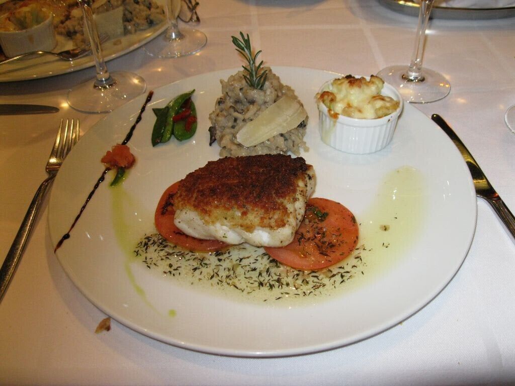 Une assiette de nourriture comprenant un morceau de poisson, des légumes et un petit bol de sauce.