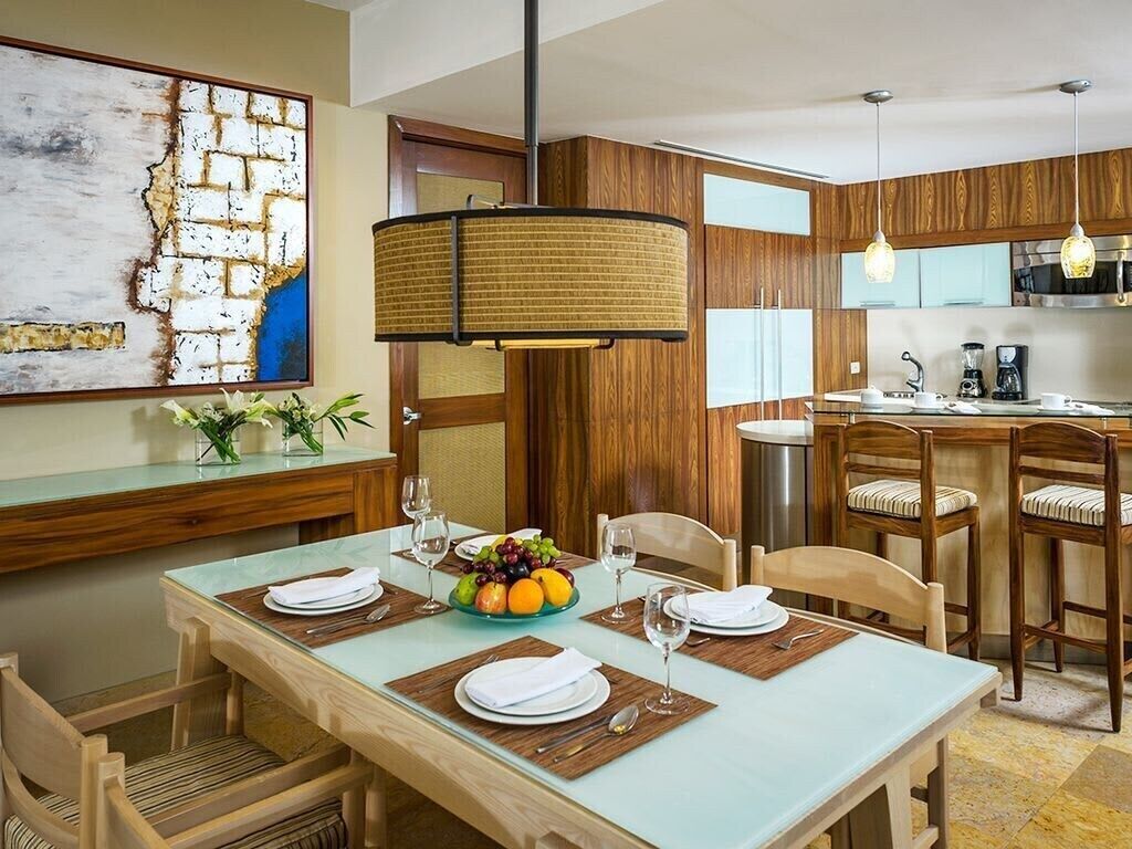 A dining area with a table set for four, a fruit bowl, and a modern pendant light.