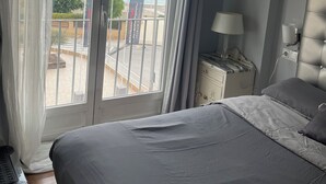 A bedroom with a large bed, a nightstand with a lamp, and a view of the sea through a sliding door.