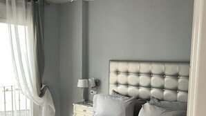 A bedroom with a bed, a ceiling fan, a nightstand, a lamp, and a window with curtains.