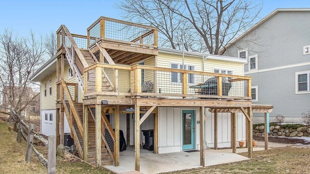 A two-story house with a wooden deck and a staircase leading to the upper level. - Sandcastle Muskegon Beach Cottage (Muskegon)