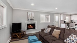 A living room with a fireplace, a television, and a sofa with cushions. - Sandcastle Muskegon Beach Cottage (Muskegon)
