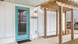 A house with a turquoise door, a wooden pergola, and a sign reading "SANDCASTLE". - Sandcastle Muskegon Beach Cottage (Muskegon)