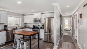A modern kitchen with white cabinets, stainless steel appliances, and a wooden table. - Sandcastle Muskegon Beach Cottage (Muskegon)