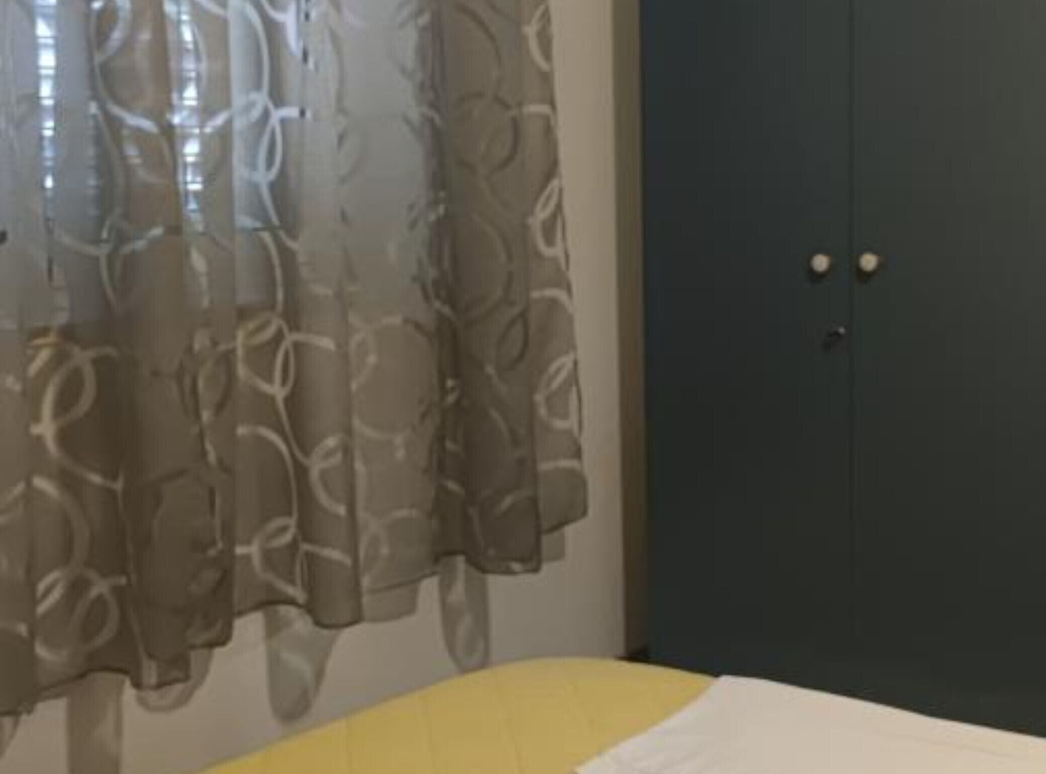 Una habitación con cama, armario y ventana con cortinas de gasa.