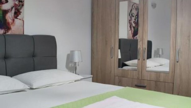 Un dormitorio con una cama, un edredón verde, un armario de madera y un espejo.