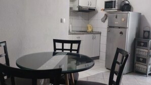 Cocina compacta con armarios blancos, microondas y refrigerador. Hay una mesa redonda de vidrio con cuatro sillas.