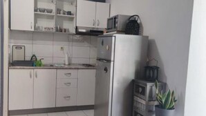 Una cocina compacta con armarios blancos, un refrigerador, un microondas y una planta en maceta.
