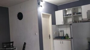 Cocina compacta con armarios blancos, una pequeña encimera y una puerta que da a otra habitación.