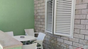 Un pequeño espacio al aire libre con una mesa y sillas, un muro de ladrillo y una ventana con contraventanas.