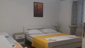 Habitación individual con piso de madera, una mesita de noche, lámpara, ventana con cortinas y un cuadro en la pared.