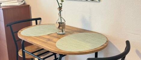 Una mesa de madera con dos individuales tejidos, sillas negras, un jarrón con flores amarillas y un espejo en la pared.