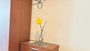 A wooden cabinet with a vase containing a yellow flower, a smartphone on top, and a chair in the background. - Apartments Villa Mira Roso - Studio Apartment 3 (Makarska)
