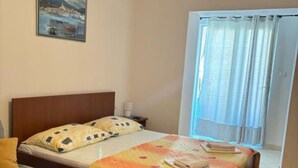 A bedroom with a bed, a nightstand, a lamp, a chair, and a window with curtains. - Apartments Villa Mira Roso - Studio Apartment 3 (Makarska)