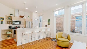 A modern kitchen with white cabinets, stainless steel appliances, and a central island with bar stools. - The Daily Condo 201 at ATB (Asheville)