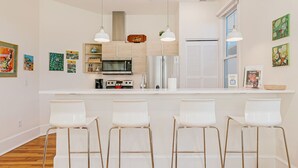 A modern kitchen with a central island, white bar stools, and pendant lighting. - The Daily Condo 201 at ATB (Asheville)