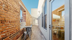 A narrow outdoor corridor with a brick wall on one side and a glass door leading to a room with a bed and a table. - The Daily Condo 201 at ATB (Asheville)