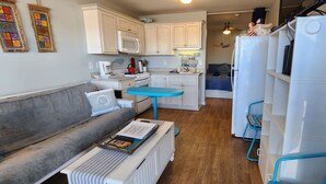 A compact living space with a kitchenette, a sofa, a small dining table, and a refrigerator. - Cozy studio with AC, WiFi, pool and is just steps from the beach! (Atlantic Beach)
