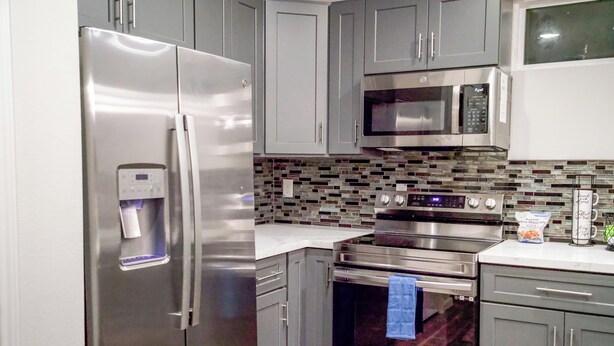 A modern kitchen with stainless steel appliances, grey cabinets, and a tiled backsplash. - Urban Oasis Retreat - Unit # 1 & 2 (Houston)