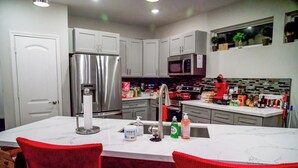 A modern kitchen with white cabinets, a stainless steel refrigerator, a microwave, and a sink with a red faucet. - Urban Oasis Retreat - Unit # 1 & 2 (Houston)