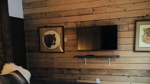 A bedroom with a wooden wall, a bed with dark bedding, a mounted TV, and framed pictures.