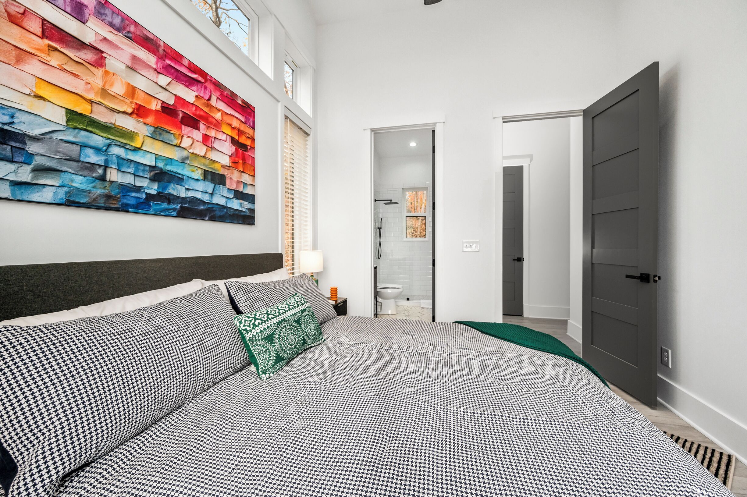 Un dormitorio moderno con una cama grande, una obra de arte colorida en la pared y vistas al baño.